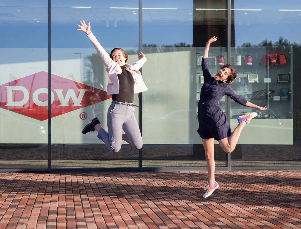 Two women jumping by Dow sign